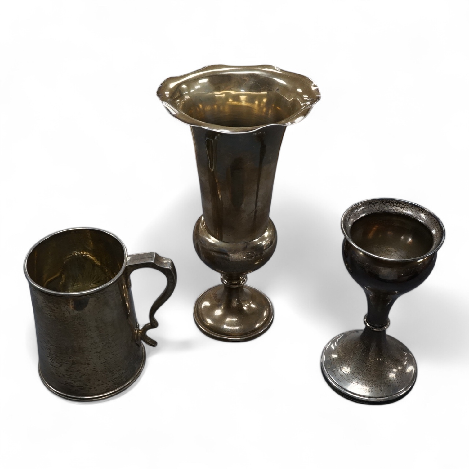 A late Victorian silver mug, with cut glass base, George Adams, London 1874, height 11.5cm, together with two silver vases, both weighted. Condition - poor to fair